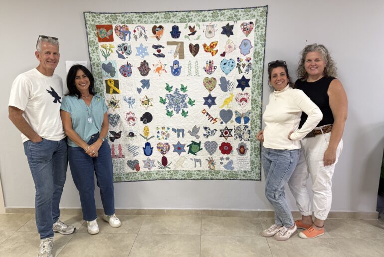 four people standing with a quilt named the quilt of hope